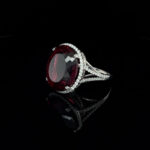 Exquisite red gemstone ring with diamond halo, set in elegant white metal.