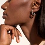 Elegant woman with radiant skin and stylish silver-black earrings against a soft backdrop.