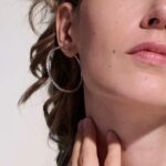 Woman with wavy brown hair and hoop earrings, showcasing natural beauty and fashion elegance.