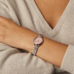 Elegant wristwatch with pink dial and polished metal band against a cozy knitted sweater.